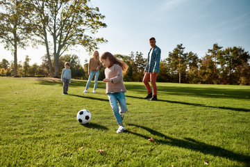 Faith, Family, Football. Happy family playing with a ball on meadow