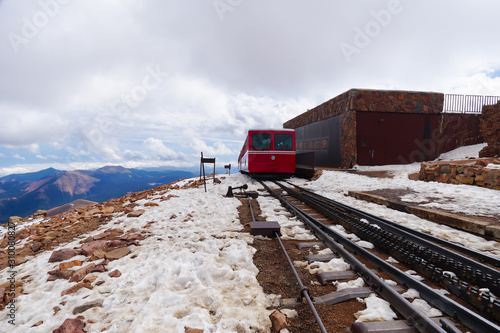 A mountain train is leaving the snow covered summit and heading back down.