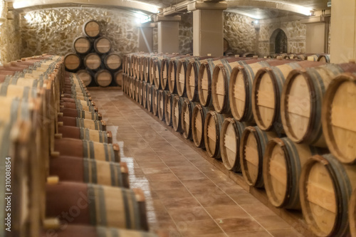 Row of old oak barrels lie on top of each other in a dry cool wine cellar in basement. Special storage for wine or other alcoholic beverages. Selective focus. Alcohol drinking culture concept.