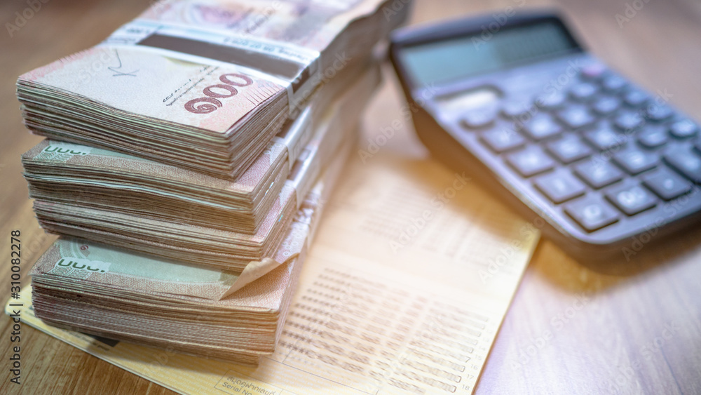 Obraz premium A lot of banknotes Along with the account book And calculator Placed on a wooden floor. Concept Saving money and financial planning or debt payment.