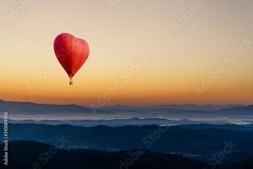 Red hot air balloon in the shape of a heart flying over the mountain