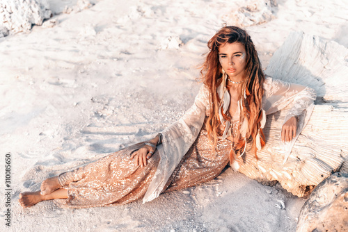 beautiful young woman in elegant dress lying on sand at the beach at sunset
