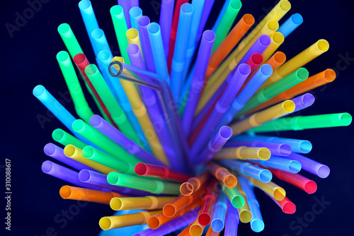 A reuseable transparent glass straw among colorful plastic straw in top view