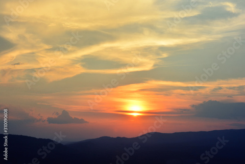 sunset sunrise in orange colors and sun over dark mountain silhouette. © njmucc
