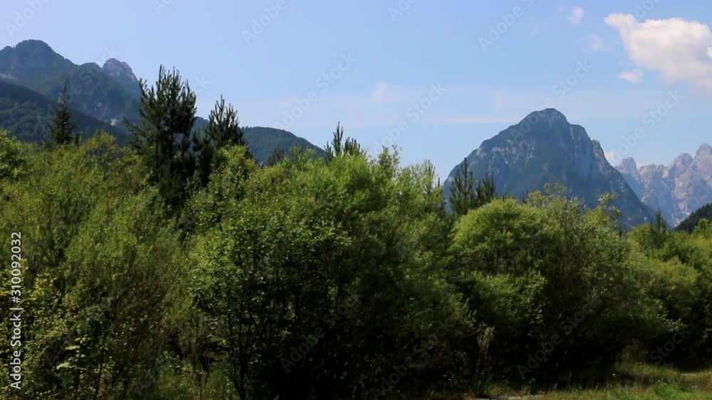 Dreamy shot of Italian Dolomites from the cycling path, looking through a row of bright green trees. Soft bright blue sky. Dreamy shot of Italian Dolomites from the cycling path, looking through a row of bright green trees. Soft bright blue sky.