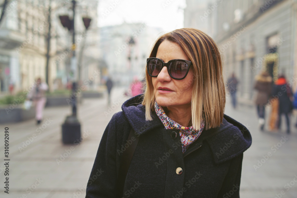 Portrait of caucasian woman wearing winter coat and sunglasses while walking the street of the city in winter or autumn morning