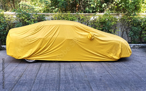  A car with a protect covered.  Yellow sheet on the pavement. 