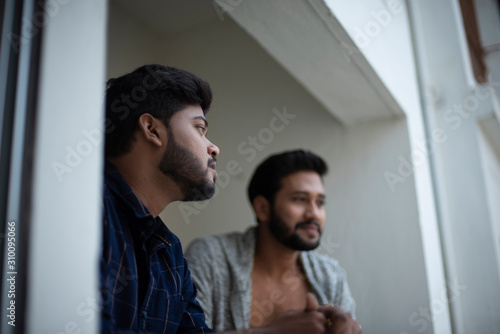 Two young tall, dark and handsome Indian Bengali men in western jackets and shirt spending time together standing on balcony in white background. Indian lifestyle.
