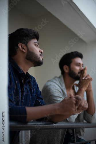 Two young tall, dark and handsome Indian Bengali men in western jackets and shirt spending time together standing on balcony in white background. Indian lifestyle.