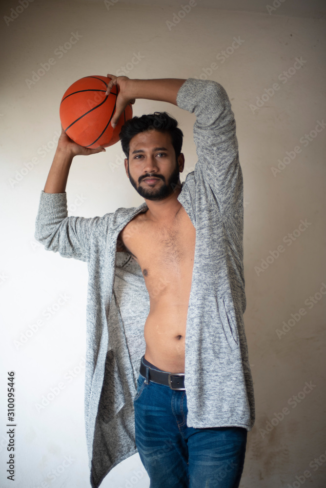 An young tall, dark and handsome Indian Bengali man in a front open western  jacket and jeans with basket ball in white background. Indian lifestyle and  fashion. Stock Photo