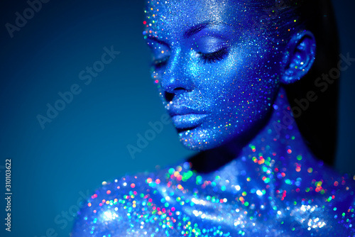 Fashion model woman in blue bright sparkles and neon lights posing in studio.  Portrait of beautiful sexy woman. Art design colorful glitter glowing make up