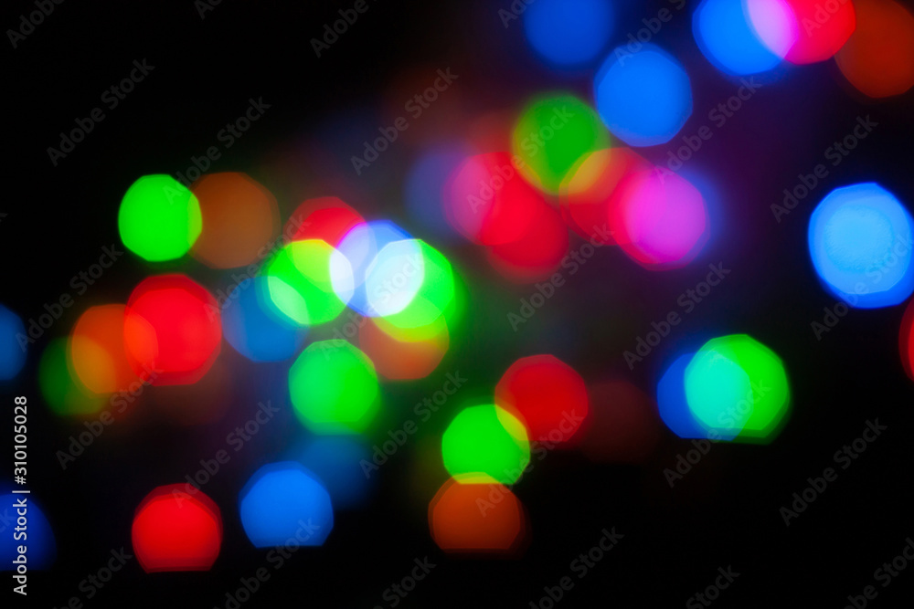 Abstract unfocused background - colorful bokeh of different bubbles on a black background. Modern blurred pattern for design and for Christmas, New year and funny holiday backdrops..