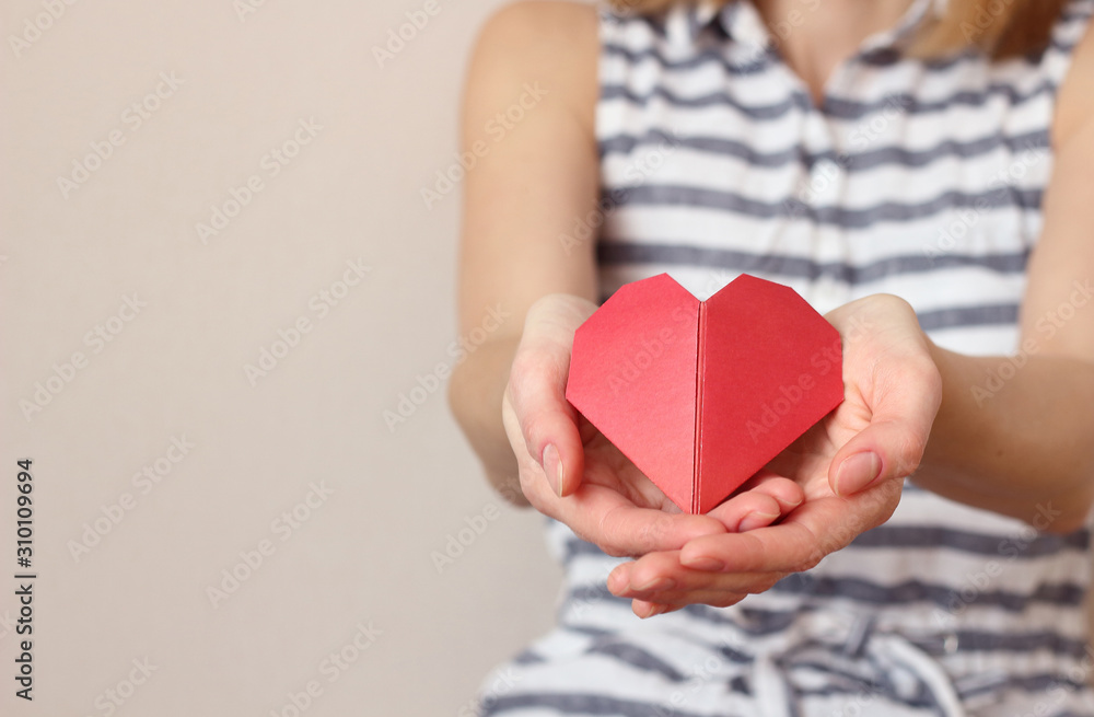 caucasian woman folds her hands in the shape of a heart and holds an origami paper heart,  insurance, charity donation concept. Place for text copy space, selective focus