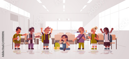 schoolboy being bullied sitting on floor surrounded by classmates mix race schoolchildren taking photo mocking boy peer violence and bullying concept classroom interior flat full length horizontal