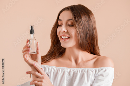 Beautiful young woman with bottle of cosmetics on light background