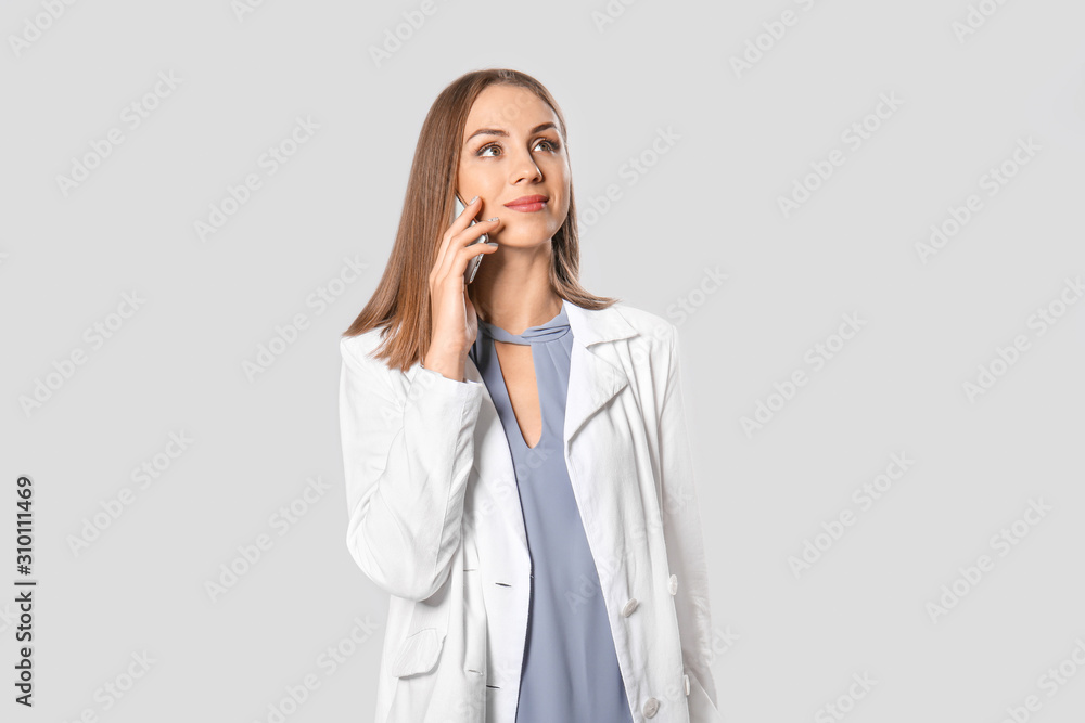 Beautiful young businesswoman talking by mobile phone on grey background Beautiful young businesswoman talking by mobile phone on grey background