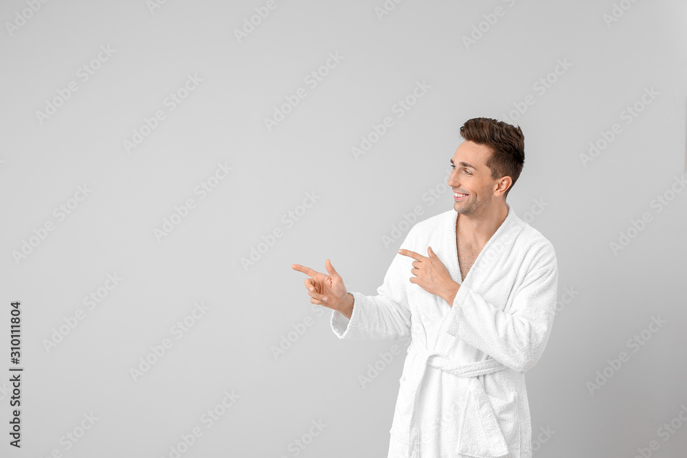 Handsome man in bathrobe pointing at something on grey background Handsome man in bathrobe pointing at something on grey background