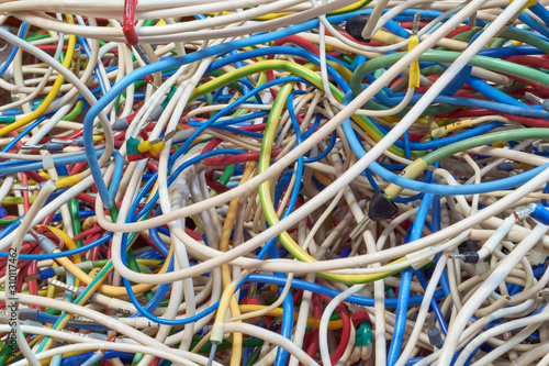 The bunch of electric wires of different colors are very much intertwined. On tangled wires is wire-end ferrules and markings. Chaos, confusion, tangle. Abstract background.