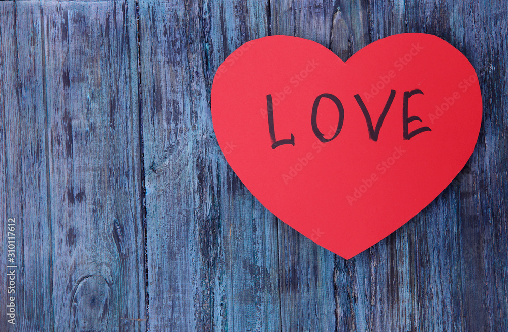 Background Valentine's Day. On a blue wooden background a red heart made of paper with the inscription LOVE. A lot of free space. STYLE FLAT LAY. Background Valentine's Day. On a blue wooden background a red heart made of paper with the inscription LOVE. A lot of free space. STYLE FLAT LAY.