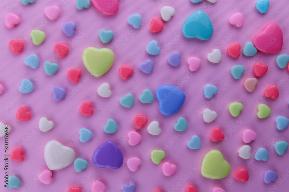 Background Valentine's Day. Yellow, blue, red and white hearts of different sizes on a pink background. Top view, close-up, cropped shot, horizontal.