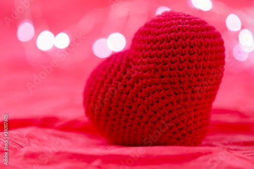 Valentine s day background. Big red knitted heart on a red background with garland lights. Side view  close-up.