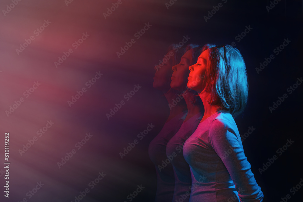 The concept of psychology and perception. The woman stands in profile, eyes closed, against a black background. Blue and red light. Copy space - obrazy, fototapety, plakaty 