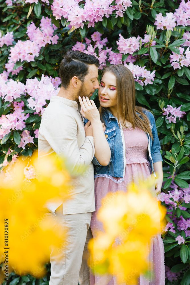 Fototapeta premium A loving couple kissing in the flowering gardens of rhododendron. Tenderness and love in a relationship. Valentine's day