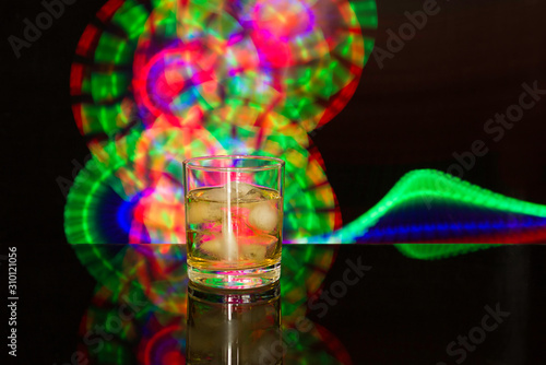 A glass of whiskey and ice on a background of colored light. Party, bar concept