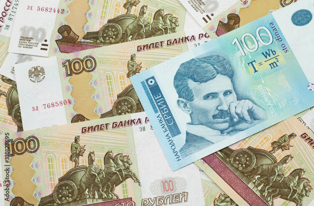 A close up of a blue and white, one hundred Serbian dinar bank note on a background of Russian one hundred ruble bank notes