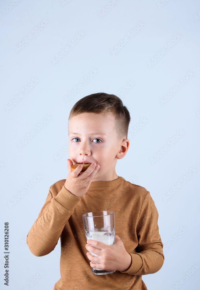 A beautiful little boy is isolated on a gray background. boy with a glass of milk and delicious cookies. A beautiful little boy is isolated on a gray background. boy with a glass of milk and delicious cookies.