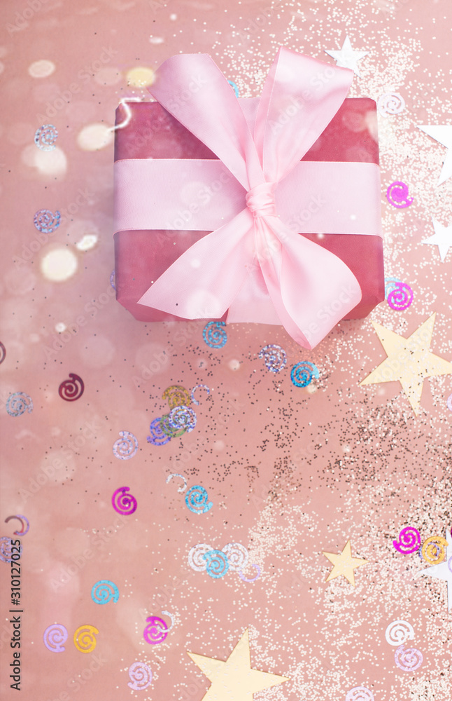 Beautiful gift box with satin ribbon in delicate colors and sparkles on a pink background.