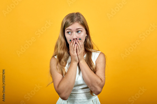 Scared young woman in fashion white shirt over isolated orange background, covering mouth with hands, looking frightened. Lifestyle concept