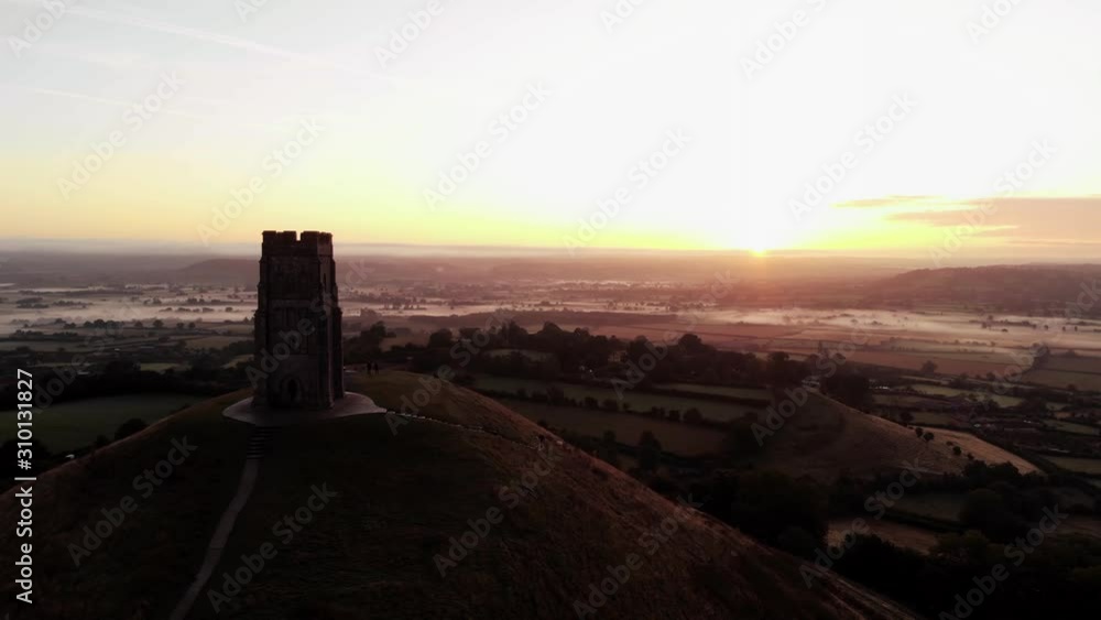 Panning aerial of the beautiful sunrise over Glastonbury Tor and the misty fields below. Panning aerial of the beautiful sunrise over Glastonbury Tor and the misty fields below.