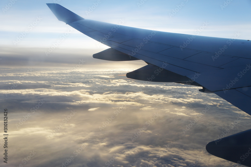 Wing of the airplane / plane seen through illuminator flying over the beautiful sunset sky and sunlit clouds. Inspirational landscape. Aircraft wings and aviation. Copy space for message. Travel. Wing of the airplane / plane seen through illuminator flying over the beautiful sunset sky and sunlit clouds. Inspirational landscape. Aircraft wings and aviation. Copy space for message. Travel.