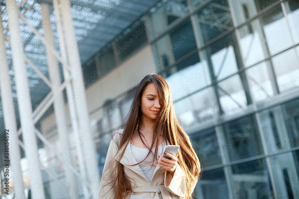 Fototapeta premium Business woman with the phone near office. Portrait of beautiful smiling female with phone, standing outdoors. Phone communication.