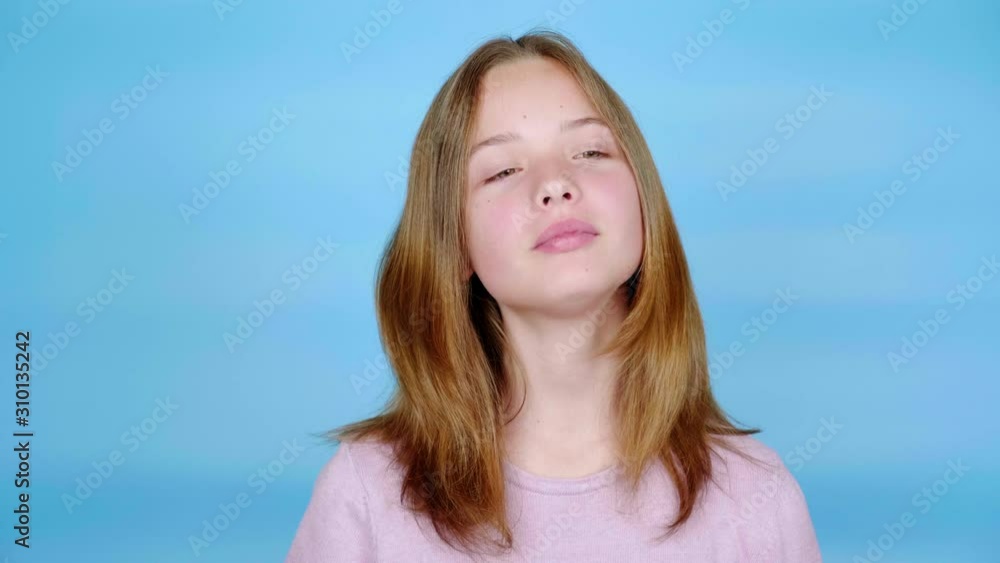 Happy teen girl in a pink pullover is smiling, takes a comb in her hand and talking. Blue background with copy space. Teenager emotions. 4k footage Happy teen girl in a pink pullover is smiling, takes a comb in her hand and talking. Blue background with copy space. Teenager emotions. 4k footage