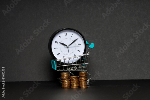 Sales. Time for Online shopping. Clock, trolley and gold coins on black background