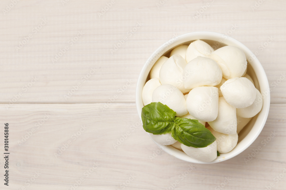 Mozzarella cheese in a bowl with basil on a wooden white table. Place for text. Mozzarella cheese in a bowl with basil on a wooden white table. Place for text.