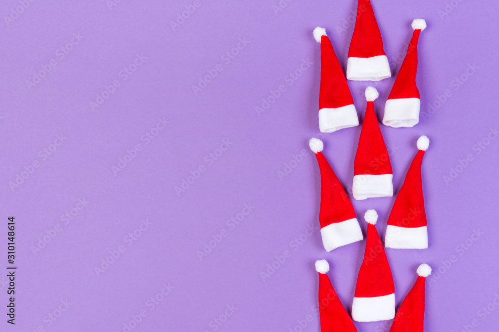 Fototapeta premium Top view od stylish red Santa hats on colorful background. Merry Christmas concept with copy space