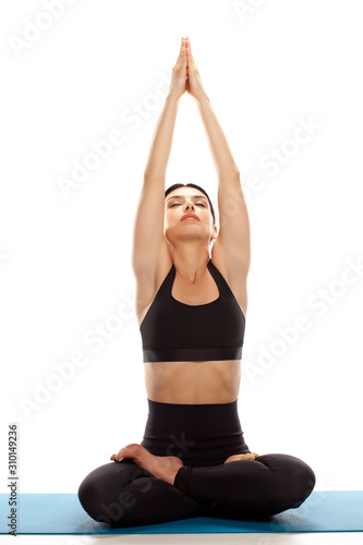Young fit yoga woman sitting down on a mat and stretching arms up. isolated on white background.