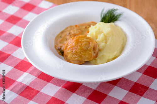 Traditional cuisine, mashed potatoes with gravy, meat and dill served on a white plate on a plaid background