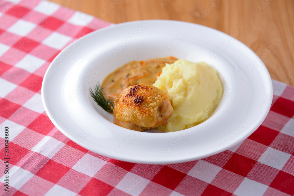 Traditional cuisine, mashed potatoes with gravy, meat and dill served on a white plate on a plaid background Traditional cuisine, mashed potatoes with gravy, meat and dill served on a white plate on a plaid background