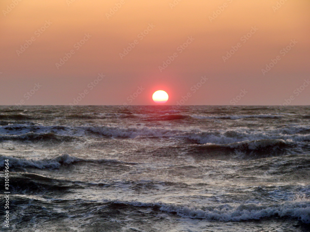 The stormy sea pushes a bright solar disk to the surface against a red-orange sky.