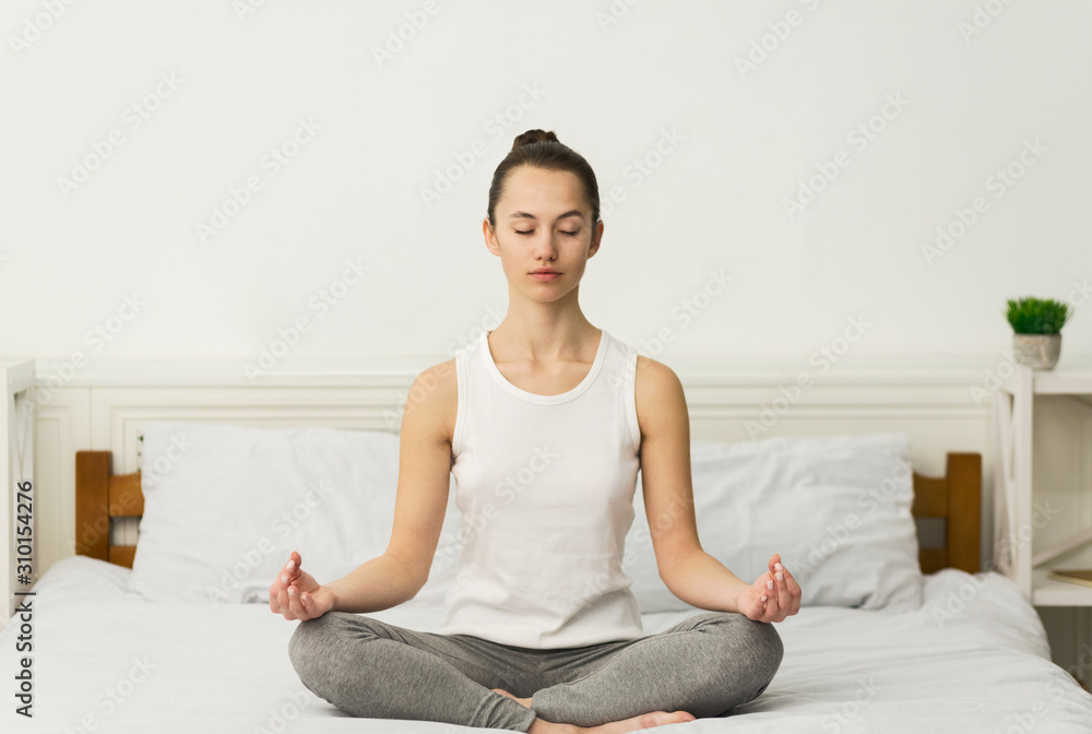 Meditation. Millennial woman sitting in lotus position on bed Meditation. Millennial woman sitting in lotus position on bed