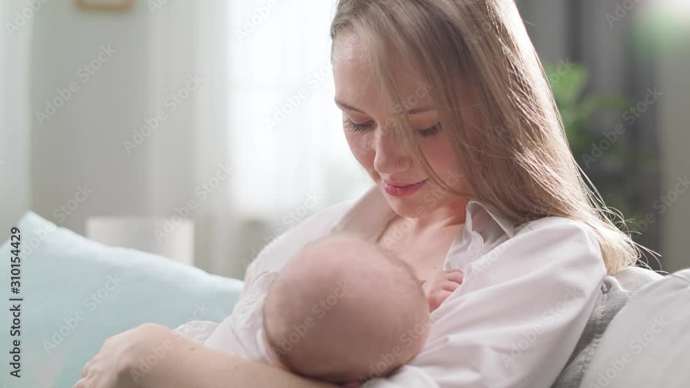 Mom breastfeeds her little daughter in the morning sun in the living room Mom breastfeeds her little daughter in the morning sun in the living room