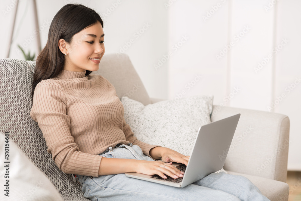 Pretty asian girl using laptop, relaxing on sofa at home Pretty asian girl using laptop, relaxing on sofa at home