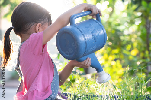 Unidentified little girl is watering her organic vegetable garden with happy moment in the background of beautiful bokeh of sunlight, concept of kid learning activity of plant and gardening.