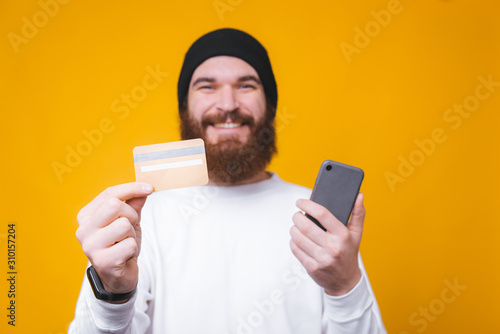 Close up ohoto of happy man shiwing his credit card and holding smartphone