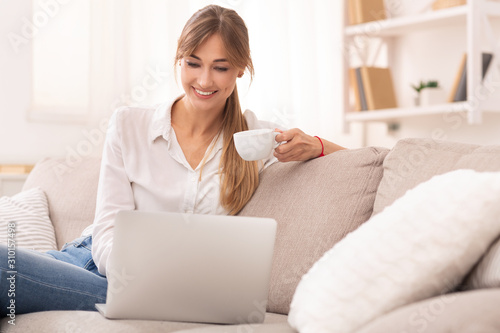 Cheerful Woman Using Laptop Having Coffee Sitting On Sofa