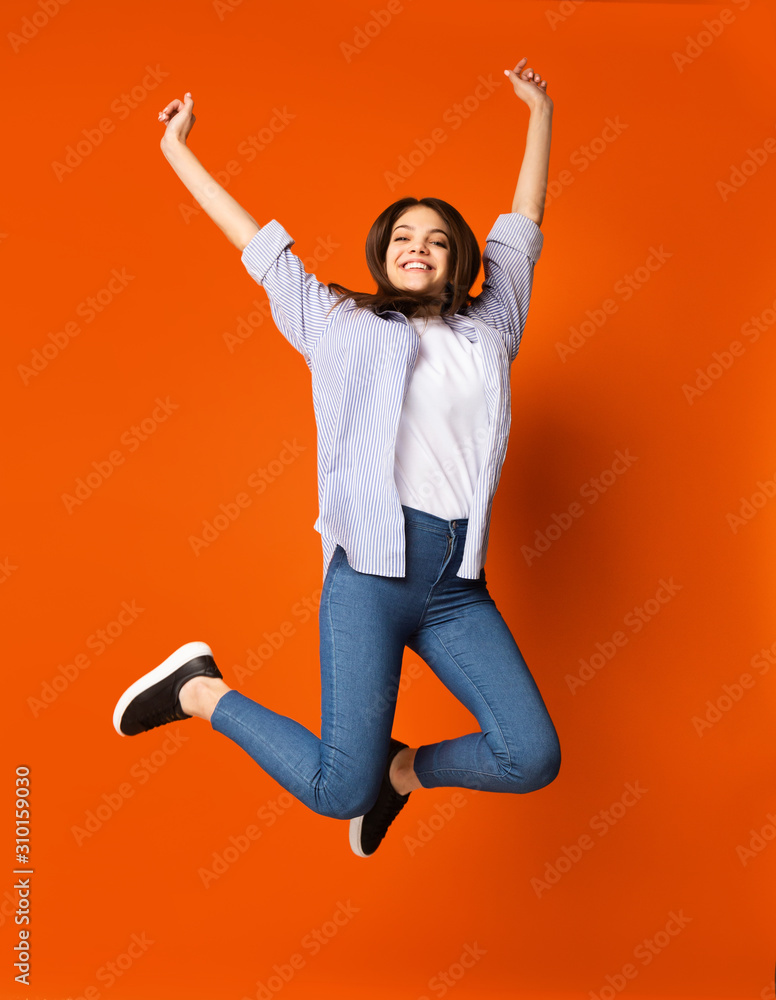 Stunning teenage girl jumping over orange studio background Stunning teenage girl jumping over orange studio background